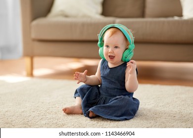 Childhood, Kids And Technology Concept - Lovely Redhead Baby Girl In Headphones Listening To Music At Home