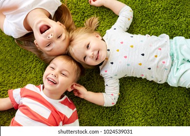 childhood, leisure and family concept - happy little kids lying on floor or carpet