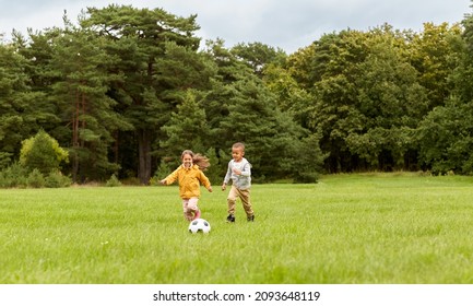 Childhood, Leisure Games And People Concept - Happy Little Boy And Girl With Ball Playing Soccer At Summer Park