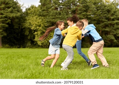 childhood, leisure and people concept - group of happy kids playing round dance at park