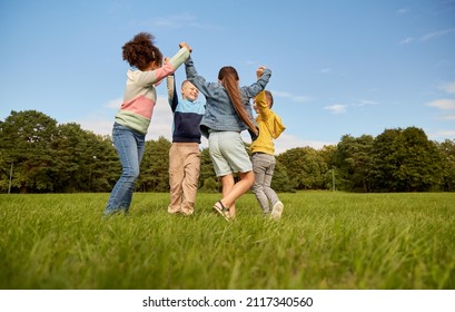 childhood, leisure and people concept - group of happy kids playing round dance at park - Shutterstock ID 2117340560