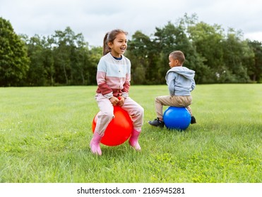 childhood, leisure and people concept - happy children bouncing on hoppers or bouncy balls at park