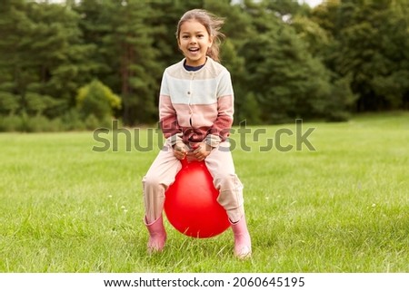 childhood, leisure and people concept - happy little girl bouncing on hopper ball at park