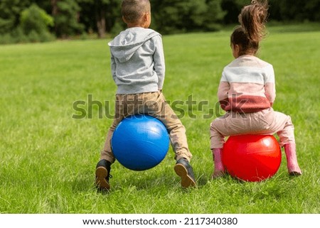 childhood, leisure and people concept - happy little boy and girl bouncing on hoppers or bouncy balls at park