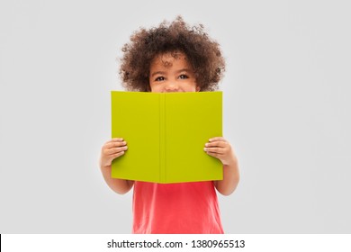 childhood, literature and reading concept - happy little african american girl with book over grey background