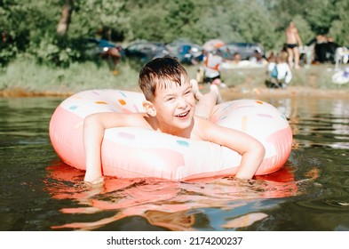 Childhood, Little Cheerful Boy Floating With An Inflatable Rubber Ring On Lake. Portrait Of Squinting Child Resting In Water On Sunny Summer Day.