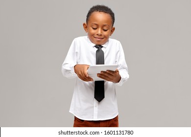 Childhood, modern technology and addiction. Studio shot of cute Afro American schoolboy addicted to electronic gadgets using digital tablet to play video games, having absorbed facial expression - Powered by Shutterstock