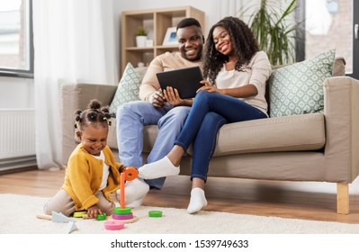 childhood and people concept - little african american baby girl playing with toy blocks and parents with tablet pc computer at home