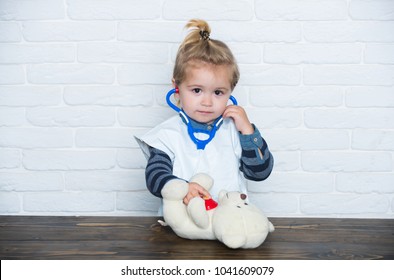Childhood, playroom, nursery. Child play doctor with teddy bear on white wall. Game, development, imagination. Future profession concept. Baby veterinarian examine toy animal with stethoscope.
