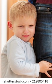 Childhood. Portrait Of Unhappy Angry Crying Blond Boy Child Kid Son Hugging Leg Of His Mother At Home. Emotions And Feelings.