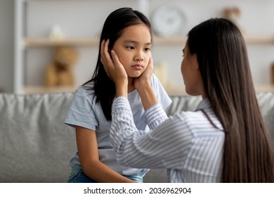 Childhood problems concept. Young mother comforting her sad offended daughter after quarrel at home. Asian woman calming down her child, sitting together in living room interior - Shutterstock ID 2036962904