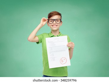 Childhood, School, Education And People Concept - Happy Smiling Boy In Eyeglasses Holding Paper With Test Result Over Green School Chalk Board Background