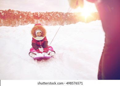 Childhood, Sledding, Leisure, Season And People Concept - Parent Carrying Happy Little Kid On Sled In Winter