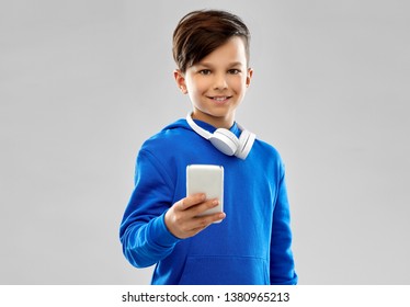 childhood, technology and people concept - smiling boy in blue hoodie with headphones on neck using smartphone over grey background - Powered by Shutterstock