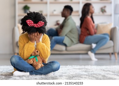 Childhood Trauma Concept. Crying Black Little Girl Sitting Alone While Her Parents Arguing At Home, Upset African American Female Kid Holding Teddy Bear And Covering Face, Selective Focus