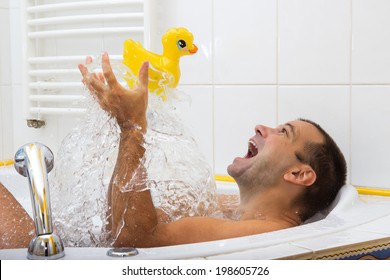 Childish cheerful man playing with toys duck in a bathtub. Playful at bathing.