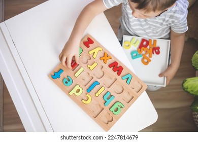 Childish hands holding alphabet wooden board with colored font letters in cells closeup. Boy girl kid arms intellect game playing early development primary education letters learning