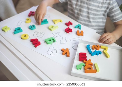Childish hands holding alphabet wooden board with colored font letters in cells closeup. Boy girl kid arms intellect game playing early development primary education letters learning - Shutterstock ID 2250055561