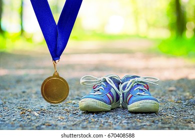 Childish Race Concept. Children's Running Shoes And Medal In Nature. 