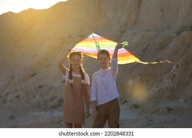 Children 8-9 Years Old Stand Under A Kite At Sunset In The Mountains.