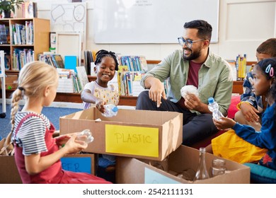 Children adding plastic bottles in plastic labelled cardboard to separate waste of the classroom at school. Primary students helping teacher arrange plastic, paper and glass in specific boxes.