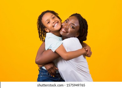 Children Adoption Concept. African American Mother Hugging Her Foster Child, Yellow Studio Background. Copy space