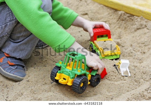 Children in air in the warm season. A\
child plays with plastic building toy cars in the\
sand.