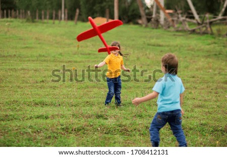 children - a boy in a blue T-shirt and a girl in yellow play a foam plastic toy red plane in nature