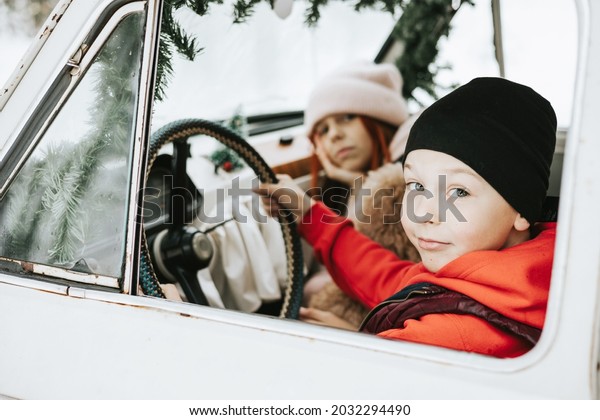 Children boy and girl with\
a dog driving a retro car decorated for Christmas among the winter\
forest in the village, the concept of a family Christmas and winter\
holidays