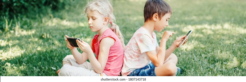 Children Boy And Girl Friends Play Games On Smartphones Outdoor. Kids Digital Gadget Screen Addiction. Contemporary Problem Of Loneliness Together. Web Banner Header For Website.