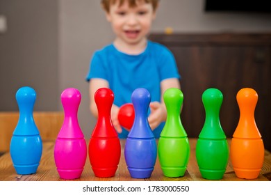 Children A Boy Throws Ball Into A Home Bowling Alley And Smashes The Bowling Pins. Selective Focus. Concept Of Active Play In The Home Room, Quarantine, Self-isolation, Achieving Goal