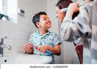 Children are brushing their teeth in the bathroom at home. The mother is checking the little boy's mouth to make sure he has brushed properly. 