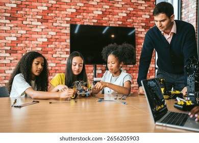 Children build and program robotics kits with teacher supervision in a modern classroom. STEM education encourages creativity, problem-solving, teamwork, and hands-on tech learning experience.
