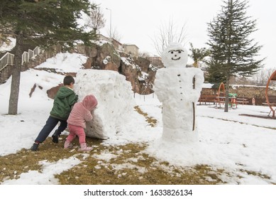 Children Build Snowman. Kids Building Snow Man Playing Outdoors On Sunny Snowy Winter Day. Boy And Girl Play Snow Balls. Winter Clothing For Baby And Toddler.