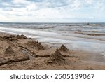 Children building sandcastles on a beach with gentle waves under a cloudy sky in summer