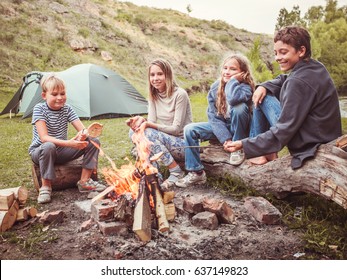 Children In The Camp By The Bonfire. Group Teen Outdoors At Summer