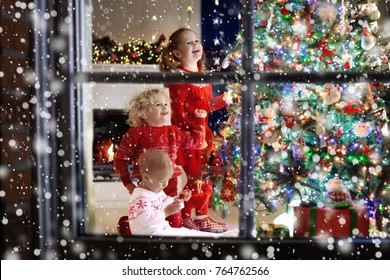 Children At Christmas Tree And Fireplace On Xmas Eve. Family With Kids Celebrating Christmas At Home. Boy And Girl In Matching Sweater Decorating Xmas Tree And Opening Presents. Holiday Gifts For Kid.