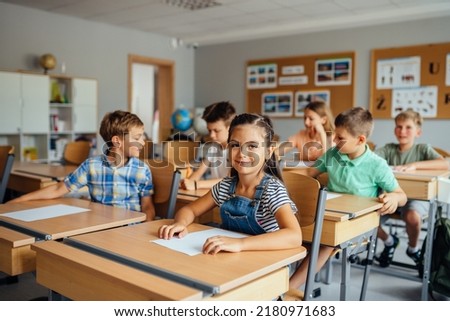 Children in the classroom at the lesson. Young cute hispanic girl looking at the camera. Classmates doing test tasks at school.