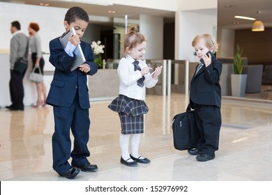 Children with communication devices in the business clothing in the business center with with adults in the background