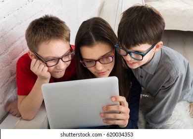 Children Computer Games, Social Networks And Media Addiction Concept. Group Of Kids In Eye Glasses Look Into Tablet. Girl And Boys With Tablet.