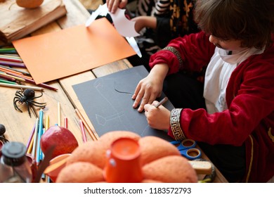 Children In Costumes Making Halloween Decorations Out Of Colored Paper In Kindergarden