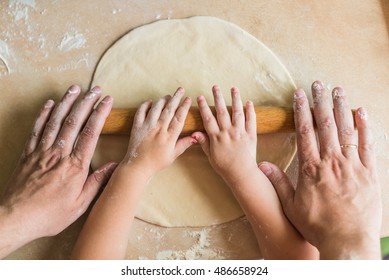 Children and dad hands rolled dough with a rolling pin on the table - Powered by Shutterstock