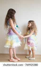 Children Dance At Home. Two Little Girls, Two Sisters Hold Hands And Dance Together. Girls Wearing The Same Dress. Two Girls With Long Hair. Home Holiday.