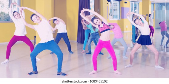 Children dancing synchronous group choreography with female coach in dance hall