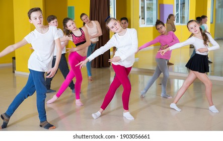 Children dancing synchronous group choreography with female coach in dance hall