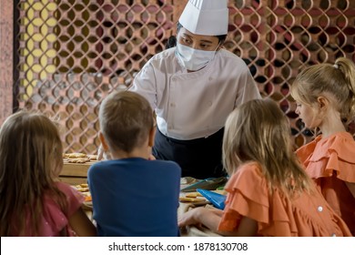 Children Decorating Christmas Biscuits And Gingerbread Cookies In Kitchen Together With Chef. Kids Cooking Class. Merry Christmas And Happy Holidays Concept