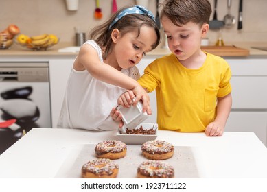 Children decorating doughnuts with colorful splashes in the kitchen at home - Powered by Shutterstock