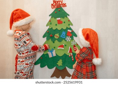 Children decorating a felt Christmas tree together in festive attire during the holiday season - Powered by Shutterstock