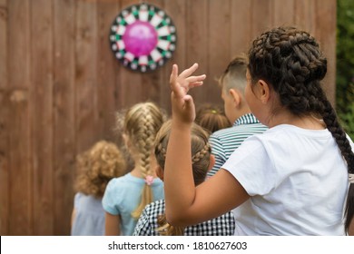 Children Of Different Ages And Heights Stand Behind Each Other, Waiting For Their Turn To Play Darts. Group Activities In Nature. Copy Space, Back View