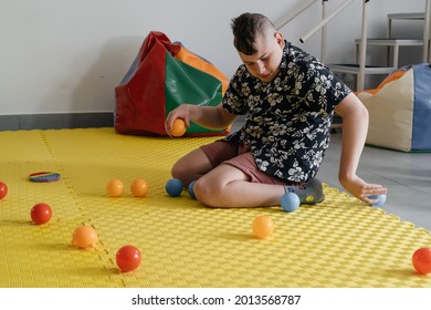 Children with disability getting sensory activity with toys, balls, small objects, cerebral palsy boy playing calming game, training fine motor skills. Rehabilitation center with therapist, mother
